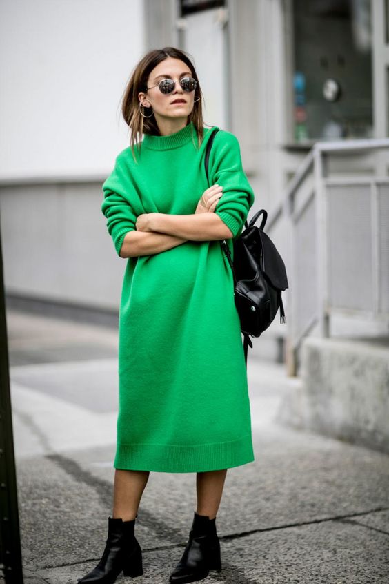 modelka w dzianinowej sukience z długimi rękawami w modnym kolorze mocnej zieleni i pasującymi czarnymi sztybletami i skórzanym plecakiem zarzuconym na jedno ramię